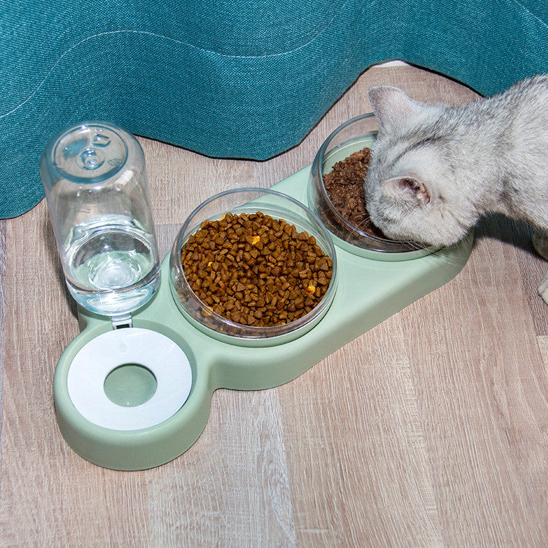 Cat eating from a green pet feeder with water and food bowls on a wooden floor.